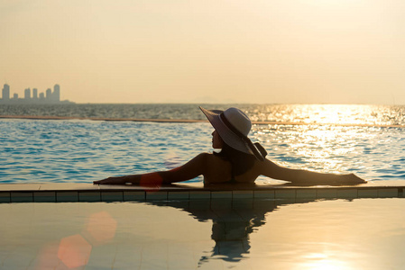 在游泳池边，在夕阳海边放松的大帽子的女人