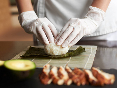 滚动寿司制作过程的特写视图。紫菜和白米在竹垫上。厨师的手摸米饭。厨师开始烹调寿司。鳗鱼和鳄梨