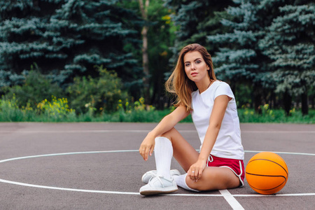 篮球运动鞋美丽的年轻金发女郎身着白色 t恤衫, 短裤和运动鞋, 坐在