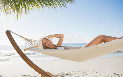 戴太阳帽和比基尼的女人在吊床上放松，对着镜头微笑