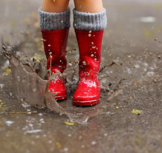 穿着红色雨靴的孩子跳进水坑里