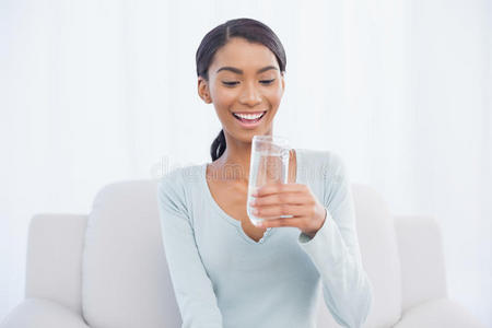 微笑迷人的女人坐在舒适的沙发上喝水