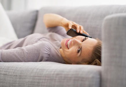 微笑的年轻女子躺在沙发上讲手机