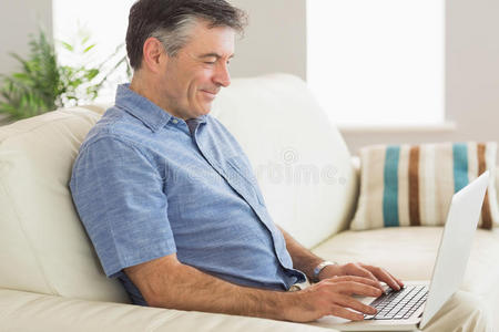 坐在沙发上用笔记本电脑微笑的男人
