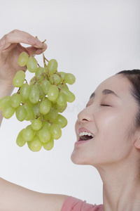 一个年轻的女人正在欣赏一束葡萄从头顶升起，摄影棚拍摄