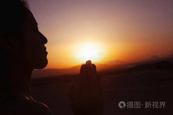 中国沙漠中双手合十祈祷的安详少女剪影落日