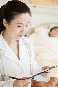 面带微笑的医生拿着病历，病人躺在病床上的照片