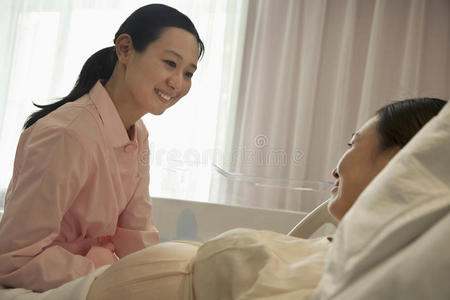 微笑的护士与躺在床上的孕妇交谈