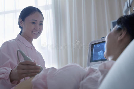 护士在医院给一位仰卧的孕妇做超声波检查