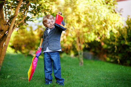 可爱的小男孩带着彩色的伞和靴子，在户外
