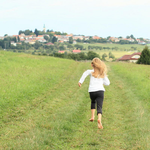 跑步的小女孩小女孩赤脚走在草坪上, 在一个温暖的阳光明媚的日子在