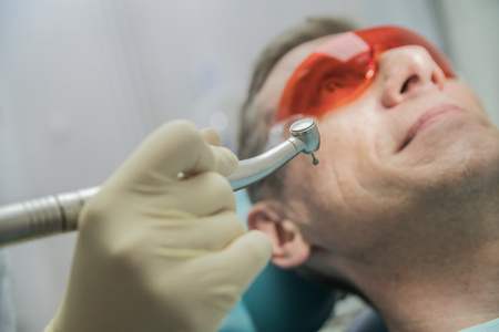 特写牙科保健概念口腔科检查。病人躺在他面前的牙医的椅子上一只手用钻