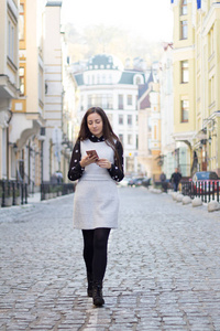 走路和在城市的街道上使用智能手机的时尚幸福女人前面观