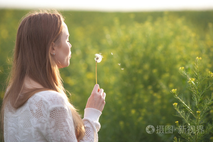 年轻春季时尚女人吹蒲公英在春天的花园.春天.