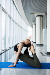 只有一条腿王鸽姿势。女人瑜伽练习构成培训概念在健身厅大窗口