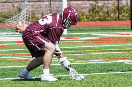 一个男性高中曲棍球运动员是在一个绿色的草皮上挖出球