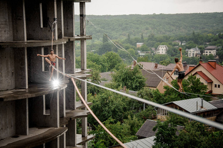 两个上身的男人在slackline的背景下,在雨天的空地上进行平衡