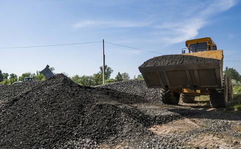 黄色装载机移动与被上传的桶在卡车用石石渣在道路建筑工程期间。道路上的石头。卸石