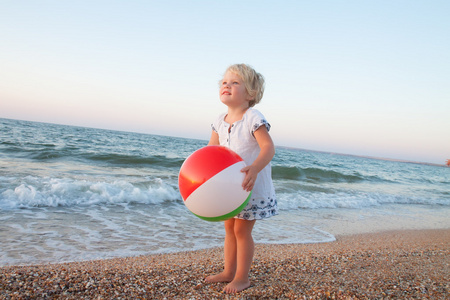 可爱的蹒跚学步的女孩，在沙滩上玩球