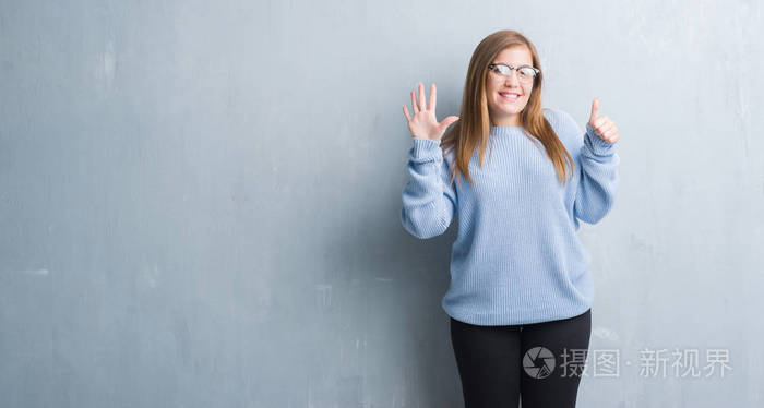 灰色垃圾墙上的年轻成年妇女戴眼镜显示和指向手指六, 而微笑着自信和快乐