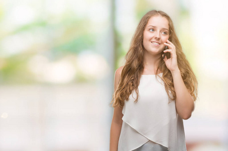 年轻的金发女郎使用智能手机与一个幸福的脸站在微笑着一个自信的微笑显示牙齿