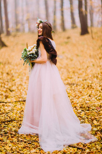 华丽的新娘与长长的黑发和花圈走在秋天的树林