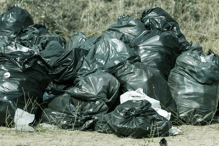 一大堆垃圾在黑色塑料垃圾袋堵塞城市公园的生态。大城市工业和生活垃圾利用的生态问题。垃圾袋