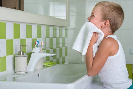 一个男孩洗脸 擦脸用毛巾在浴室里