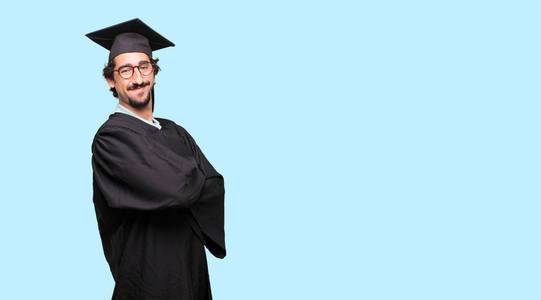 年轻的毕业男子自豪, 满意和快乐的脸上, 微笑着双臂交叉