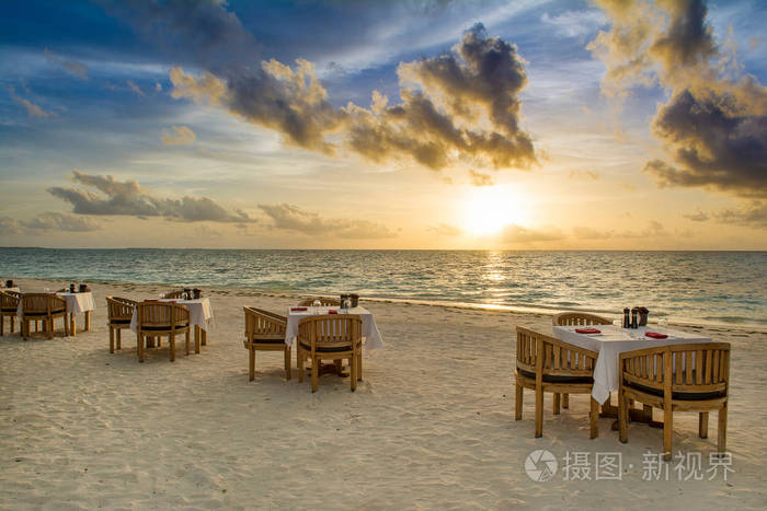 沙滩上的热带餐厅。美丽的日落在马尔代夫的海岛与五颜六色的天空和剧烈的云彩波浪海的风景