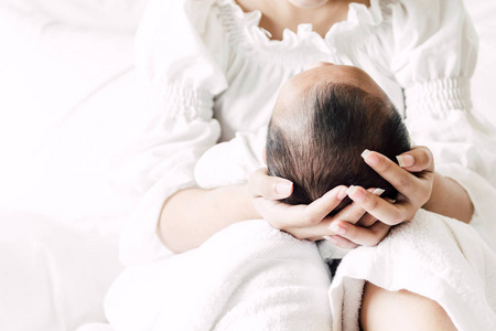 母亲抱着婴儿在她的怀里, 在一个白色的卧室.对家庭概念的爱照片