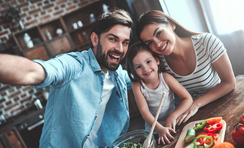 妈妈, 爸爸和女儿正在厨房做饭。幸福的家庭观念。英俊的男人, 迷人的年轻女子和他们可爱的小女儿正在一起做沙拉。健康的生活方式