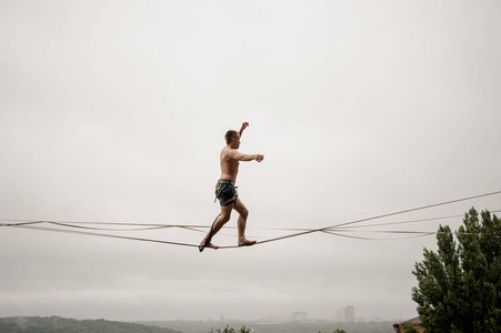 坚强勇敢的人走在slackline对灰色的天空在雨天夏天天