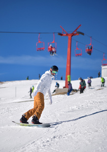 年轻男子在滑雪下坡与蓝蓝的天空和背景中的升降椅