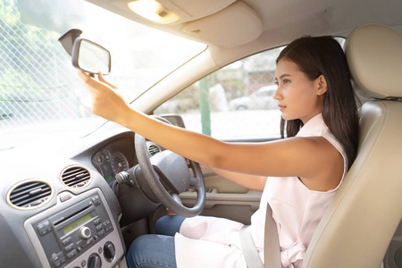 年轻女子司机用手调整后视镜, 检查化妆, 确保安全出行, 旅途驾驶理念。亚洲女孩坐在汽车座椅内