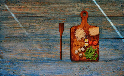 在一个木制破旧的复古餐桌是一个木板, 切蔬菜在它是一块帕尔马干酪, 鹌鹑蛋和樱桃西红柿, 在一个大的木制叉子附近
