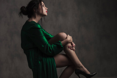 黑色的梦幻女郎的侧面看着长绿色的礼服, 抱着她的腿, 看着, 而坐在