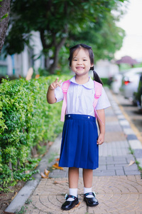 愉快的小女孩在泰国学校制服与背包站立在公园, 准备好回到学校