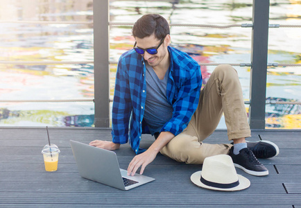 水平照片的年轻时尚的白种人的家伙在湖户外公园，聚精会神地看着他使用温暖的夏天晚上享受无线连接的笔记本电脑屏幕旁边的木制表面上