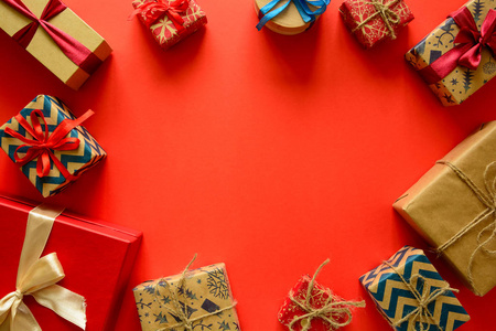 在红色纸的背景上用丝带装饰的礼品纸上的圣诞礼物的顶部视图。新年节日和庆典装饰品的概念。复制空间。平躺