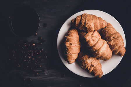 顶部视图。新鲜的牛角面包和咖啡在黑色的背景。宏拍摄。早餐的概念。甜点和咖啡。伴侣穆迪颜色