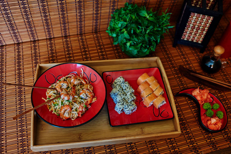 在木托盘上, 有两个红色的盘子, 在日本的风格, 一份两份鲑鱼寿司与熏鳗鱼和第二盘乌冬面与蔬菜和大虾的甜酸酱