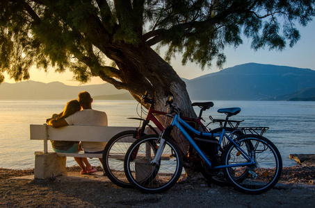 一对情侣看日落坐在海边的长椅上照片