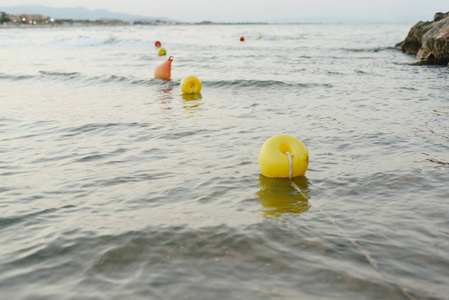 漂浮在海滩附近的浮标和海岸的岩石没有沐浴的日落