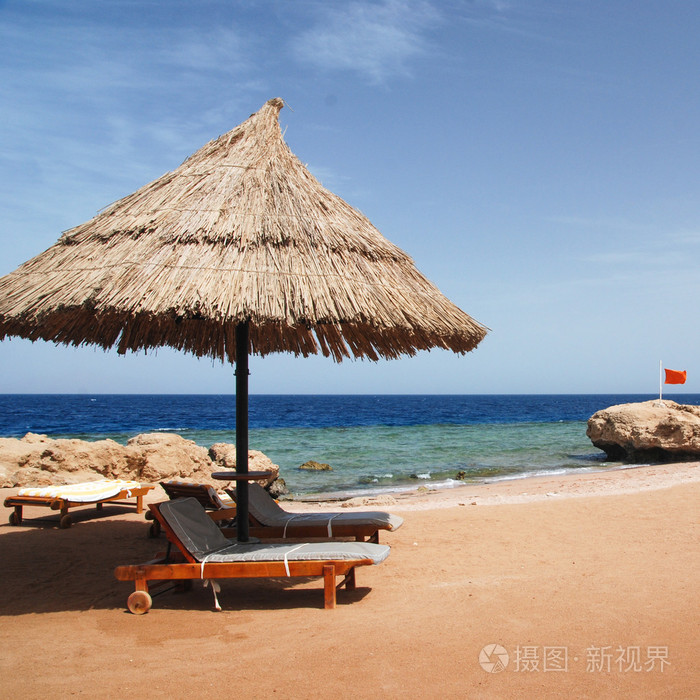 美丽清澈的绿松石海洋水面的照片, 在海景背景和遮阳伞下的日光浴躺椅上的波纹低波浪