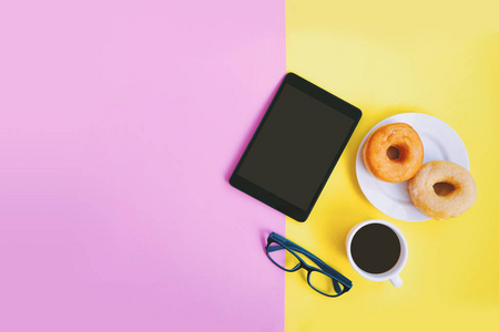 现代家庭办公工作区, 黑咖啡杯和甜甜圈, 眼睛眼镜和平板上的粉红色和黄色粉彩背景与复制空间