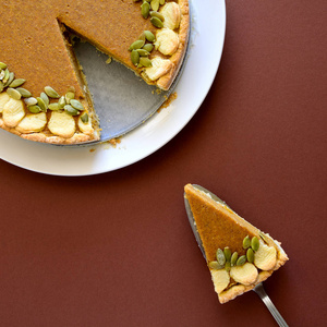 一块自制的南瓜馅饼, 上面有肉桂的褐色纸张背景。感恩节或万圣节假期的概念。顶部视图