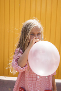 外膨胀女孩吹气球外面, 与黄色背景照片