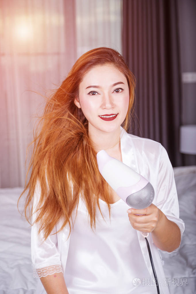 女人在卧室里柔和的光使用吹风机