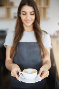 由年轻但经验丰富的女店员服务的完美拿铁艺术卡布奇诺的特写